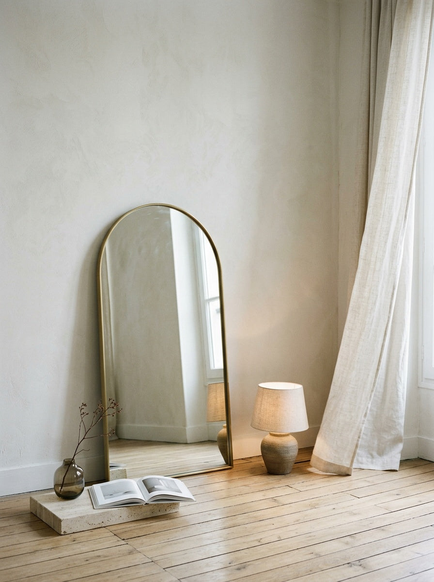 Miroir arche posé au sol près d’une lampe en céramique