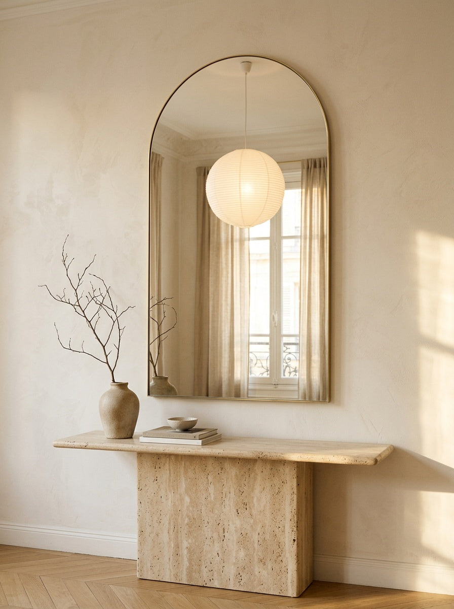 Arched mirror with a thin brass frame above a travertine console